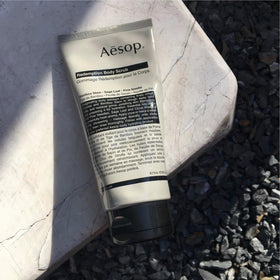 Aesop Redemption Body Scrub next to a 6.2 oz scale for accurate size and travel-friendly convenience