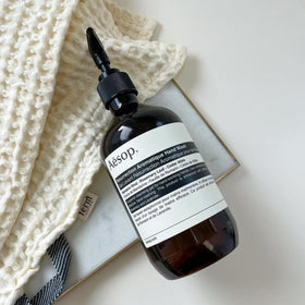 Aesop bottle held next to hand showing 16.9 oz scale and refill benefit