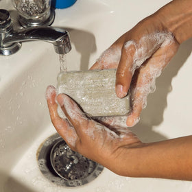 Baxter of California bar in use under shower illustrating gentle exfoliation and rinse-off ease