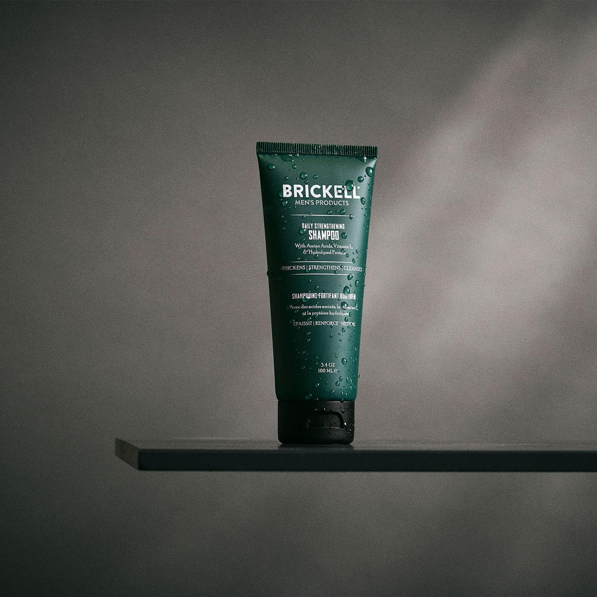 Brickell Men's Products bottle in hand under shower showing refreshing use benefit
