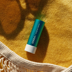 COOLA Liplux staged with beach essentials to show water-resistant use