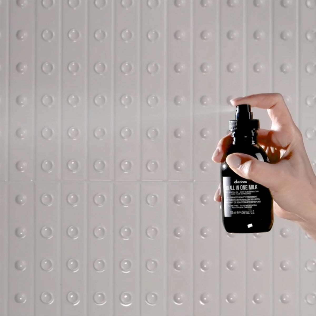 Davines OI size comparison in hand to show full-size bottles and travel milk portability