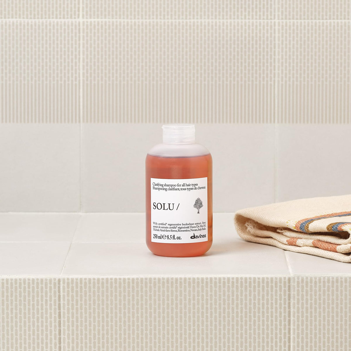 Davines SOLU/ bottle held in hand for scale showing compact 8.5 fl oz convenience