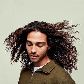 DevaCurl 12 fl oz bottle next to hand for size and scale clarity