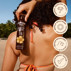 Hawaiian Tropic spray being applied on skin at the beach for hydrated tan