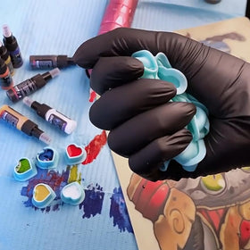 IFERO tattoo artist dipping needle into a heart ink cap showing practical in-session use