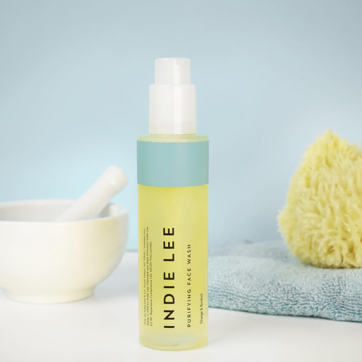 Indie Lee size scale next to hand showing compact 4oz travel-friendly convenience