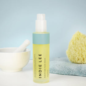 Indie Lee size scale next to hand showing compact 4oz travel-friendly convenience