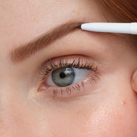 jane iredale applying pencil to brows in mirror for defined yet natural-looking shape
