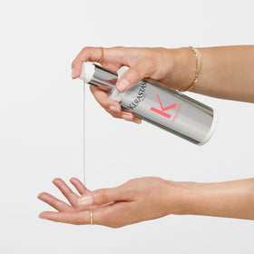KÉRASTASE bottle styled on bathroom shelf among towels to suggest salon-grade repair at home