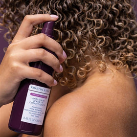 Kristin Ess bottle spraying mist onto wet hair demonstrating even application and protection
