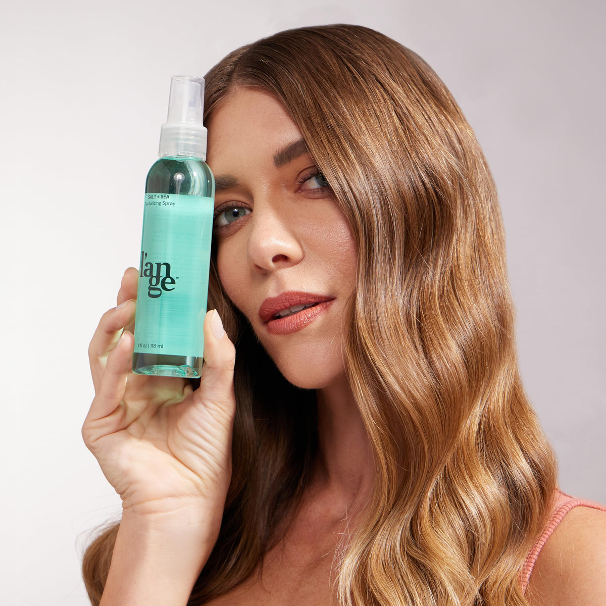 L'ANGE HAIR 4 oz bottle beside smartphone for compact, on-the-go convenience