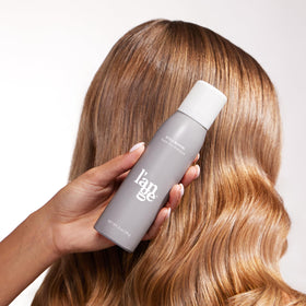 L'ANGE HAIR bottle beside hand for scale, communicates travel-friendly convenience benefit
