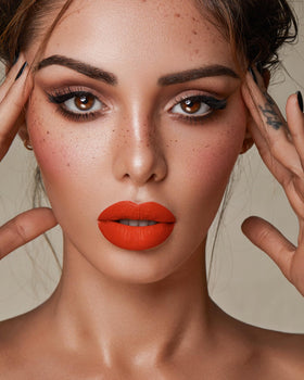 MAKI YIKA lip swatch on model illustrating vivid orange payoff and matte look
