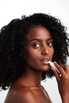 MALIN+GOETZ lip balm held in hand to show compact size and travel-friendly benefit