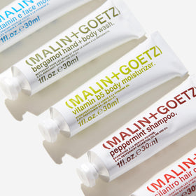 MALIN+GOETZ kit next to passport and boarding pass showing TSA-friendly sizes benefit