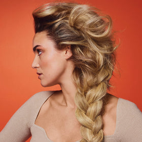 ORIBE bottle in a beach scene demonstrating UV activation and on-the-go brightening benefit