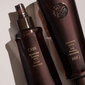 Oribe Maximista 6.8 oz bottle in hand to show scale and portable styling convenience