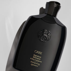 Oribe Signature Shampoo held in hand for scale and travel-friendly benefit