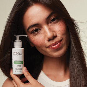 Paul Mitchell gloss drops next to ruler for scale to show compact 2.5 fl oz travel-friendly size