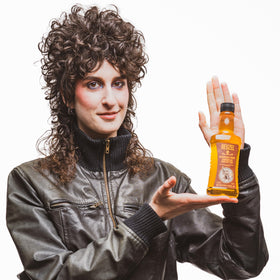 REUZEL bottle next to brush and dryer showing compatibility with heat styling tools