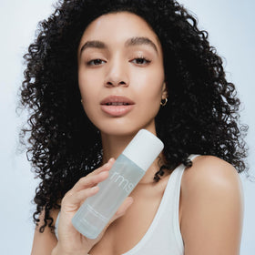 RMS Beauty bottle held next to hand to show scale and travel-friendly size benefit
