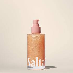 Person applying Saltair Coral Coast body oil on damp arm, demonstrates hydrated glow benefit
