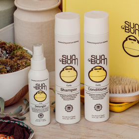 Close-up of Sun Bum formula on curly strand showing smoothing effect and added shine