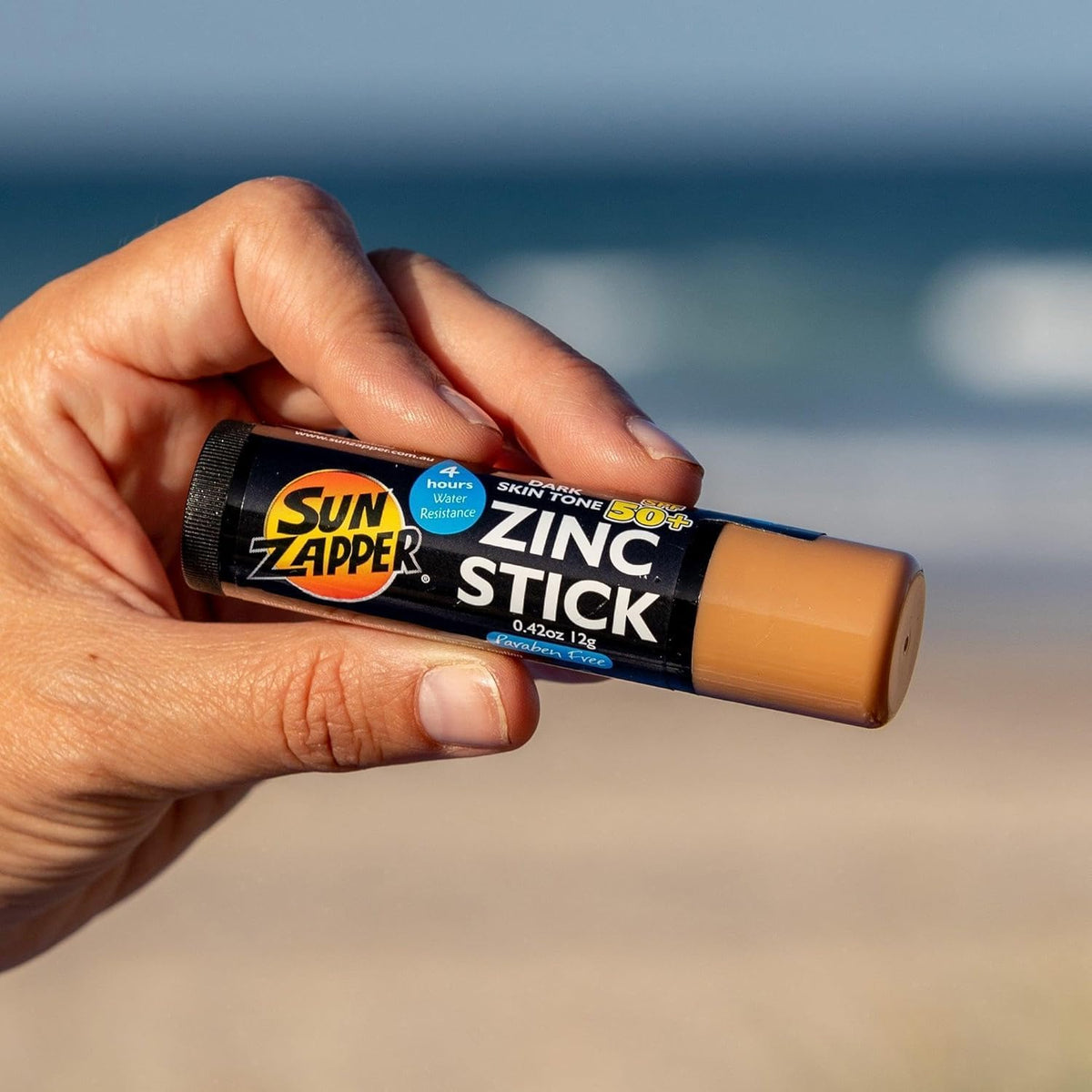 Person holding Sun Zapper stick on the beach showing quick reapplication benefit