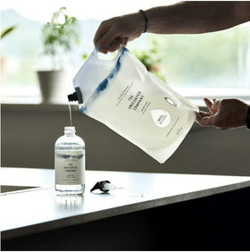 The Unscented Company pouring refill into reusable dispenser for easy refill