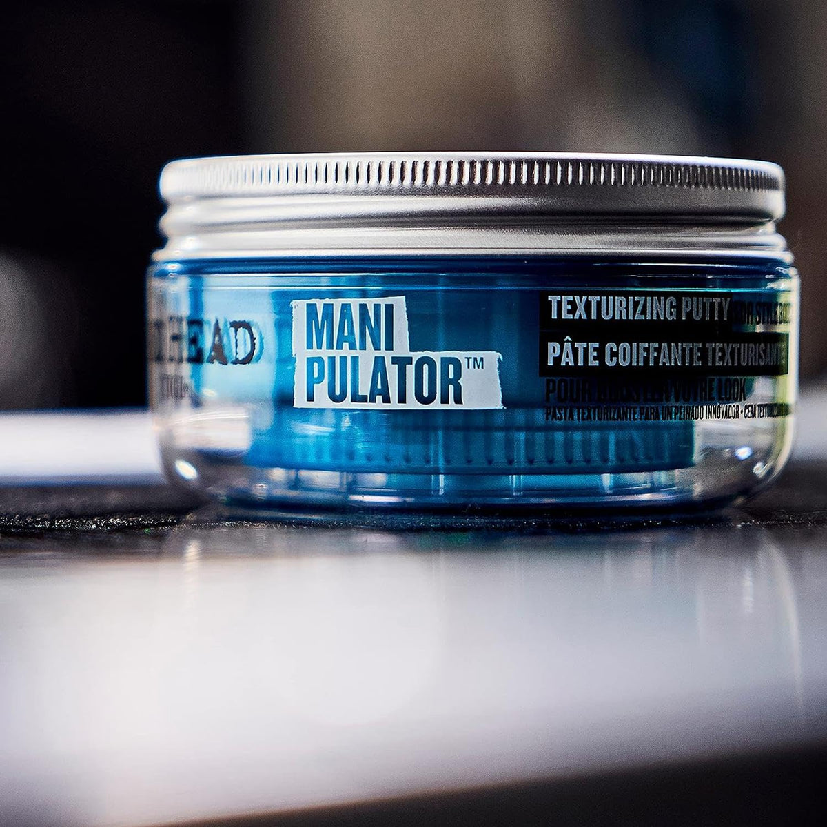 TIGI Bed Head Manipulator held in hand to show compact 2 oz scale for travel convenience