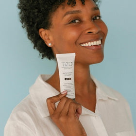 TIZO AM Replenish beside a hand for size comparison illustrating travel-friendly tube